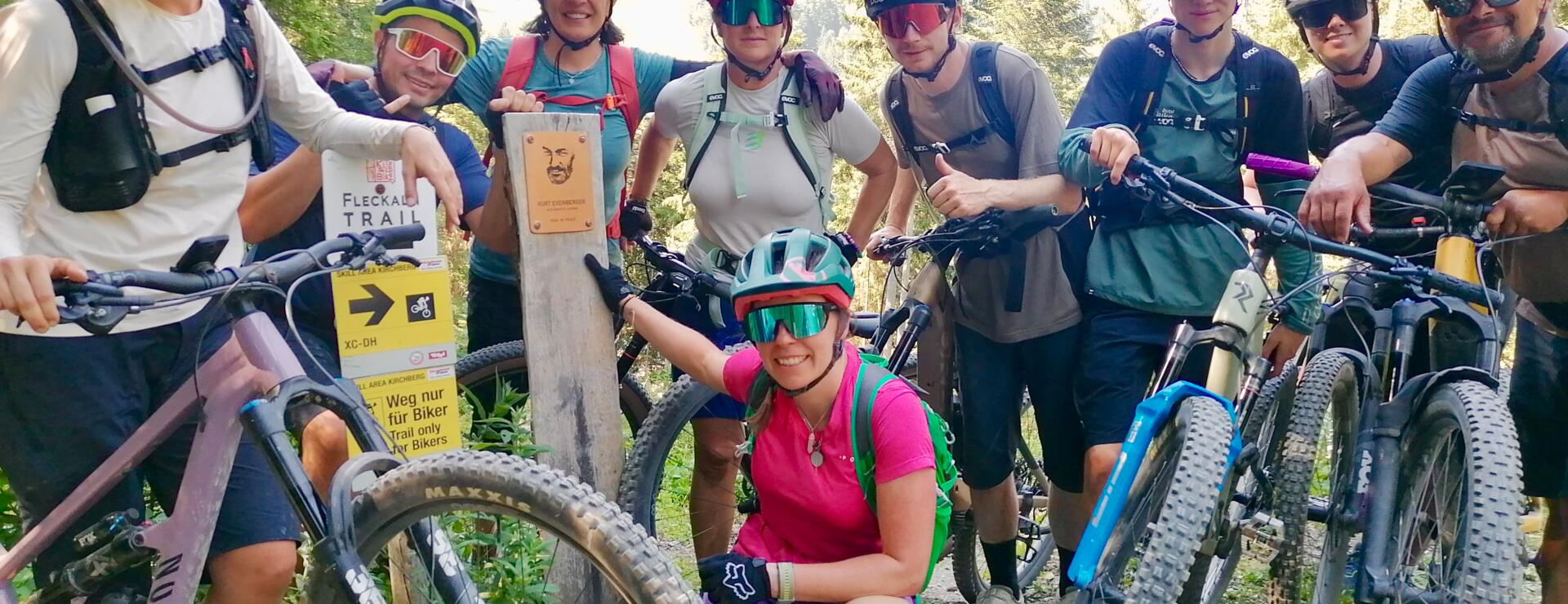 Mountainbike-Gruppe im Wald | © © Bikeacademy Eine motivierte Mountainbike-Gruppe posiert auf einem sonnigen Waldweg mit Helmen, Rucksäcken und Bikes. Die sportliche Outdoor-Szene zeigt Teamgeist, Naturerlebnis und aktive Freizeit in den Bergen.