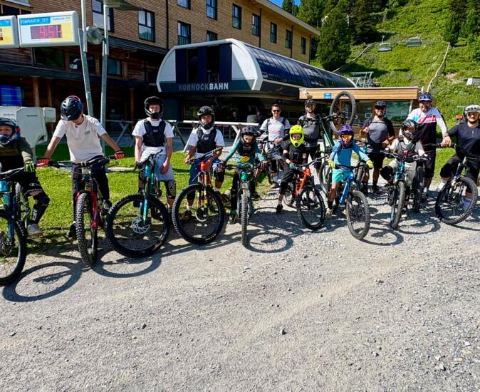 Mountainbike-Gruppe an der Bergbahn | © © bikegenuss.at Eine Gruppe junger Mountainbikerinnen und Mountainbiker steht mit Fahrrädern und Helmen vor einer Bergbahnstation. Die sonnige Szene zeigt ein sportliches Outdoor-Erlebnis in alpiner Umgebung, ideal für Bike-Camps, Fahrtechniktraining und gemeinsame Abenteuer am Berg. Turracher Höhe - Kärnten - AUSTRIA